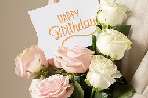 Bouquet Éclat de fête composé de roses roses et blanches tenu à la main avec une carte d’anniversaire.