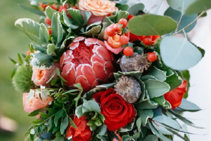 Bouquet d’union composé de protea rouge, roses corail, eucalyptus et feuillage bohème